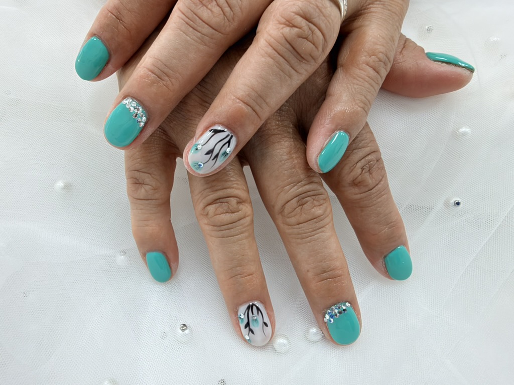Vista completa de la manicura turquesa de Miora Nail con flores negras y turquesas sobre base blanca