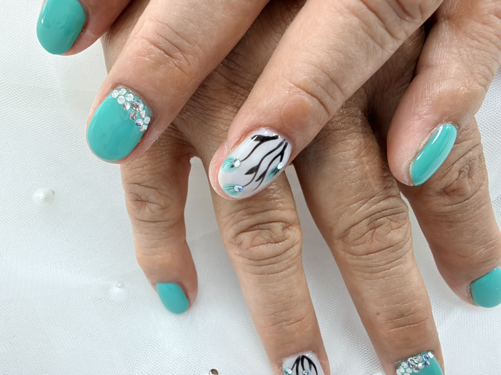 Detalle del diseño floral sobre blanco y los cristales junto a la cutícula en uñas turquesas